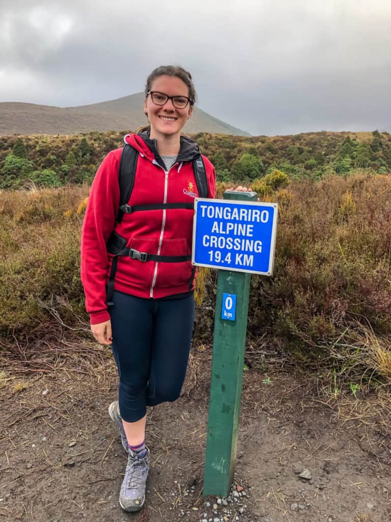 How to Hike the Tongariro Alpine Crossing and Why You'd Want To 4 Nina posing with the starting sign of 0km at the beginning of the Tongariro Alpine Crossing