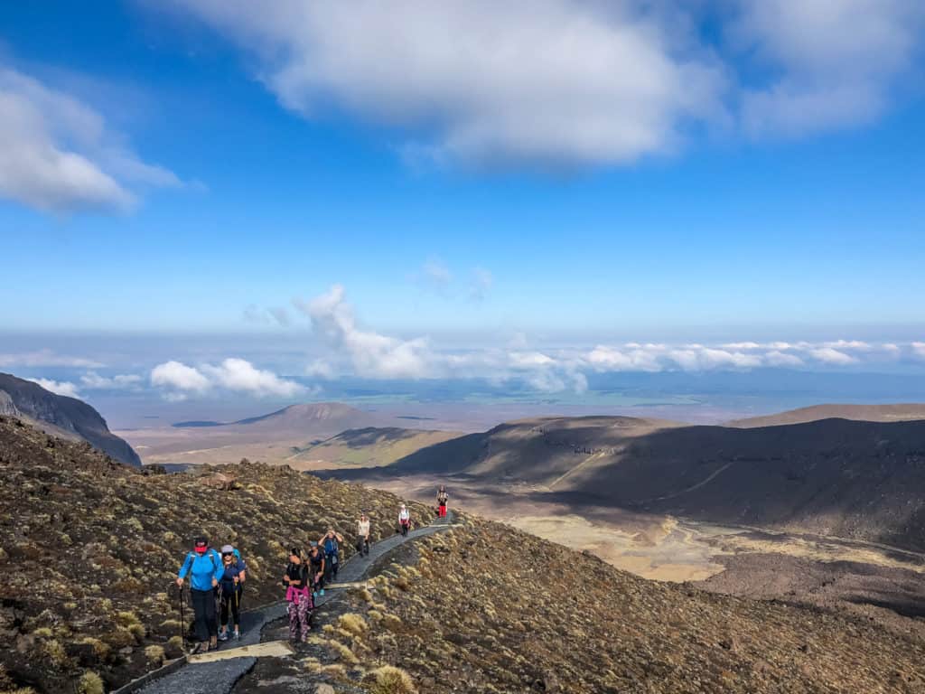 How to Hike the Tongariro Alpine Crossing and Why You'd Want To 14 The ascent up the Tongariro Alpine Crossing with hikers slowly climbing the incline and the mountains in the distance