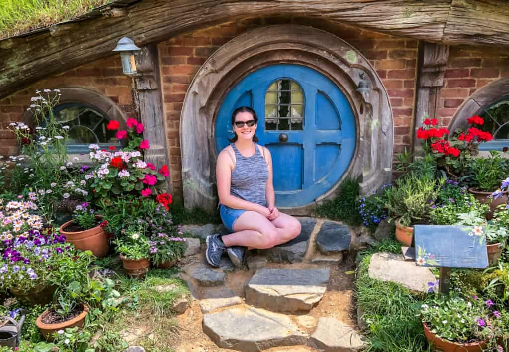 Visiting the Stunning Hobbiton Movie Set in New Zealand 15 Nina on the Hobbiton movie set tour posing in the front garden of a blue hobbit home.