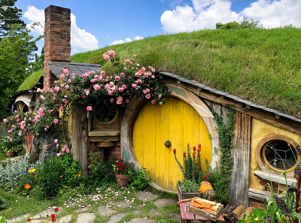 Visiting the Stunning Hobbiton Movie Set in New Zealand 12 Yellow hobbit hole door in the Hobbiton village. Brick building with a chimney and a grassy roof.