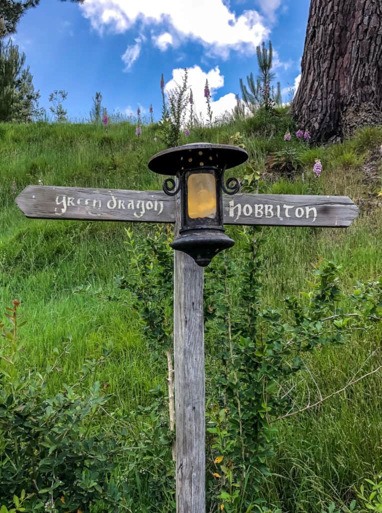 Visiting the Stunning Hobbiton Movie Set in New Zealand 14 Wooden direction sign at Hobbiton movie set in New Zealand. One direction points to Hobbiton and the other points to "Green Dragon".