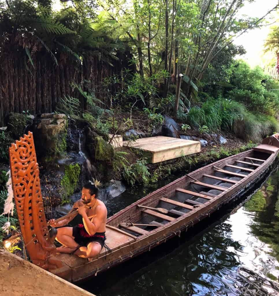 101 New Zealand Fun Facts To Know Before You Go (2024) 5 Maori man in a traditional canoe in traditional costume at Tamaki Maori Village in New Zealand.