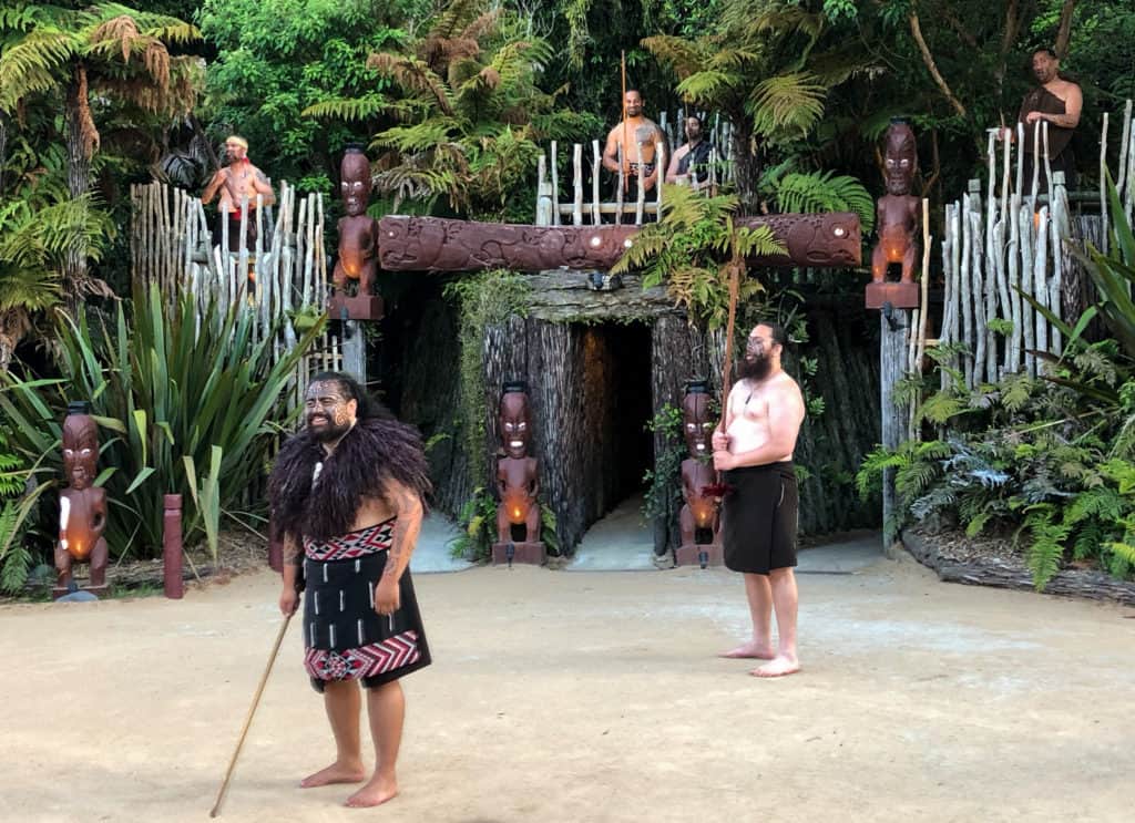 Why You Can't Miss the Tamaki Maori Village Experience in Rotorua 16 Two men in traditional Māori attire standing in front of a wooden gate at Tamaki Maori Village.