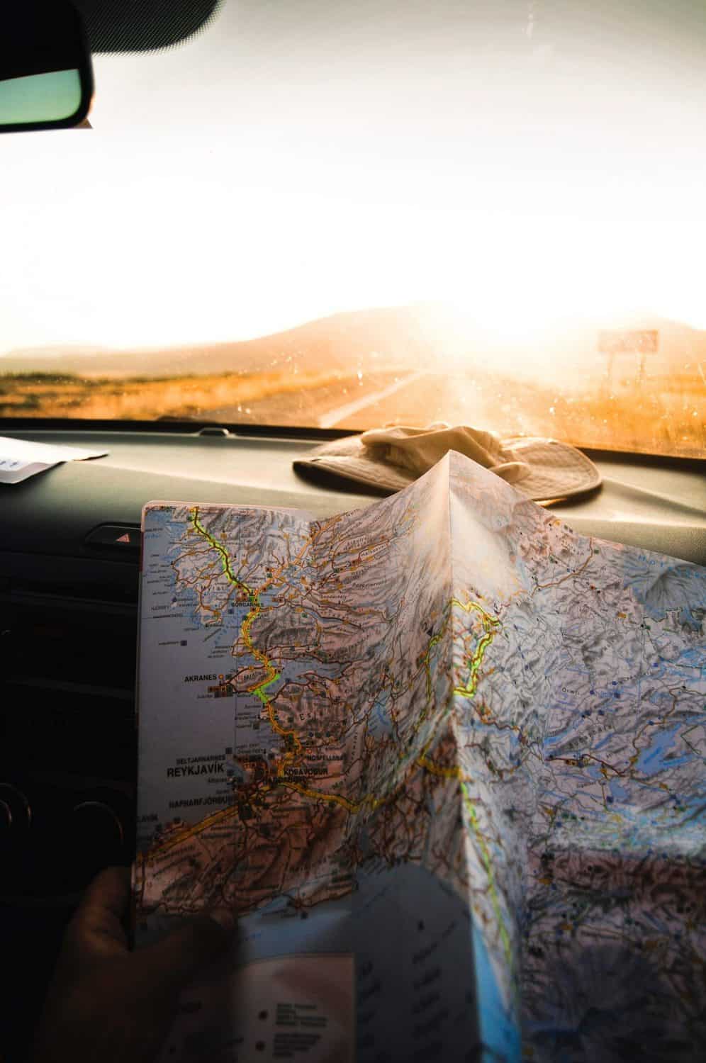 How I Travel Plan: Travel Planning Tips 5 Unfolded map on the dashboard of a car in front of a crumpled hat as the car heads into the sunset on a road trip