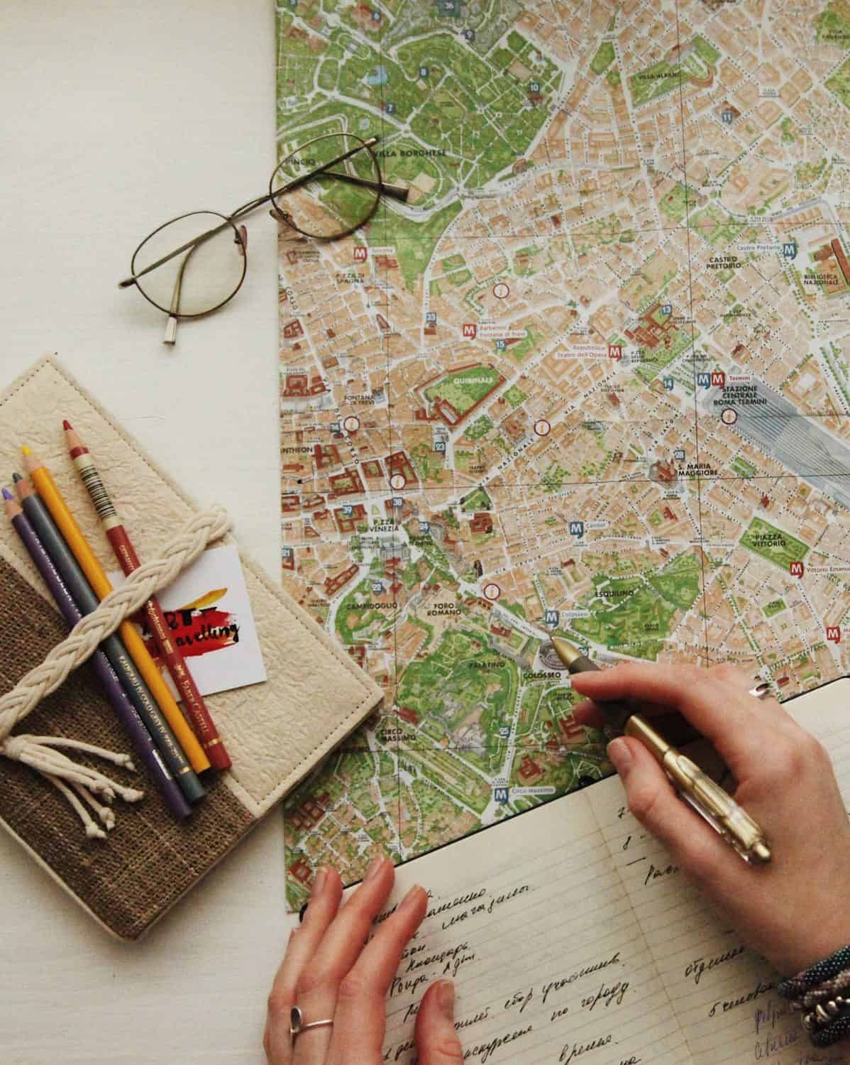 How I Travel Plan: Travel Planning Tips 2 Woman planning a travel itinerary for her trip by looking at a map and writing in a notebook