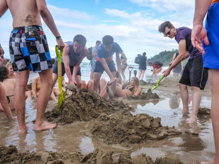 A group of people enjoying their time building sand castles on the hot water beach in New Zealand.