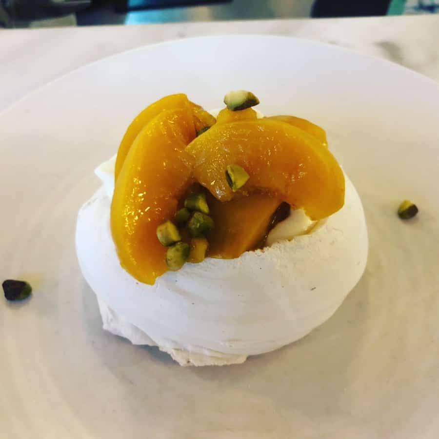 25 Pros and Cons of Living in New Zealand 4 New Zealand food represented by an image of a pavlova topped with peaches and pistachios