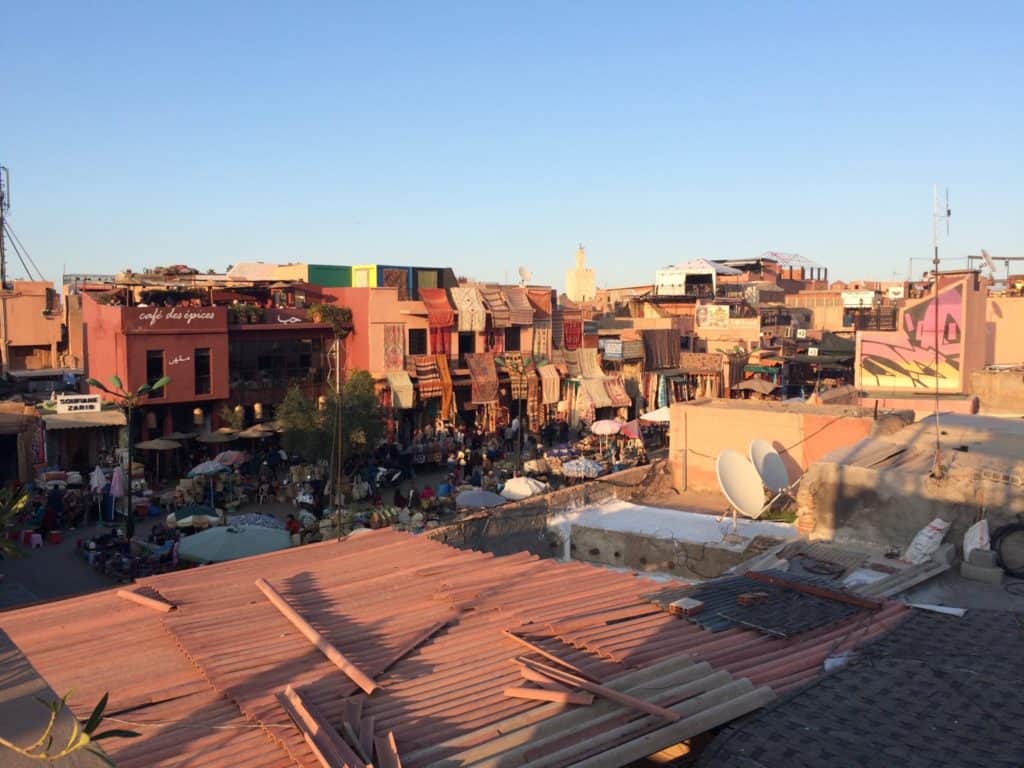 Is Marrakech Safe for Solo Female Travellers? 1 Marrakech medina rooftop view at the golden hour showing the old buildings - one with rugs draped over it - and the night market starting to get set up
