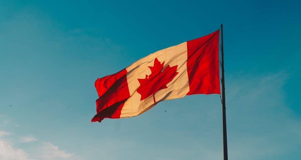 45 Pros and Cons of Living in Canada from a Canadian 16 Canadian flag flying in the wind against a teal sky