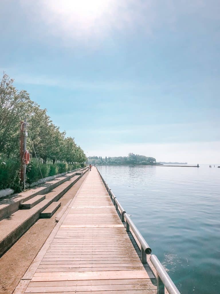 Is Toronto Worth Visiting in 2024? Local Guide 2 Toronto boardwalk with sailboats and kayaks floating on Lake Ontario beside it and the CN Tower viewed in the background