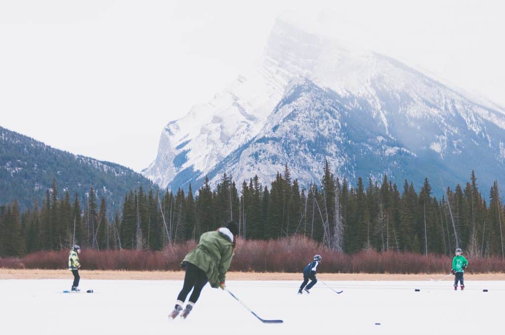 100 Essential Canadian Slang to Know Before You Visit Canada 8 Kids playing hockey on a frozen lake in Canada during the winter with a large looming mountain and pine trees in the background