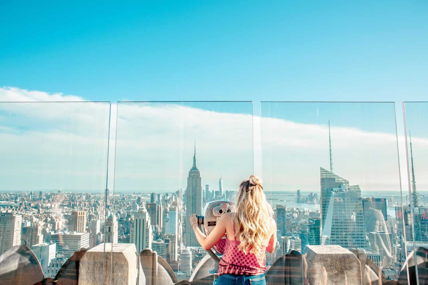 15 Unique Solo Staycation Ideas for Singles 8 Woman looking through a viewfinder on top of a building onto the New York skyline as she has a local staycation