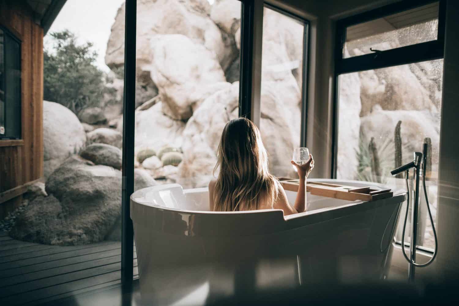 15 Unique Solo Staycation Ideas for Singles 3 Woman in a white bath tub with a glass of wine having a spa day