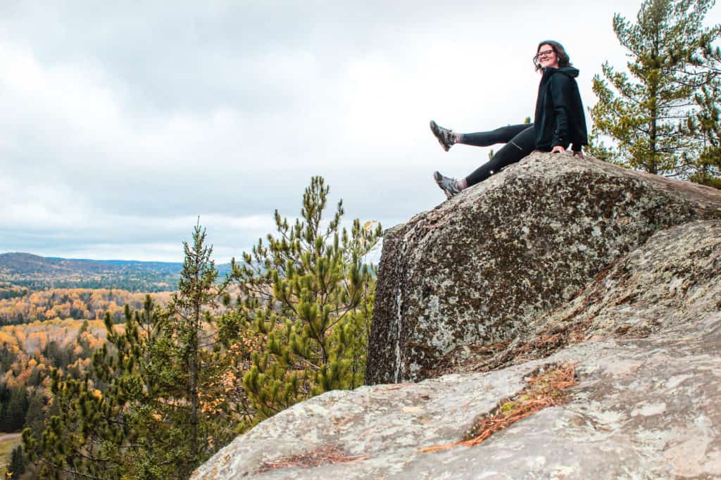 29 Greatest Ways to Make Money Travelling the World 8 Nina smiling at the camera while sitting on a cliff face in Algonquin Park at a travel blogger outing