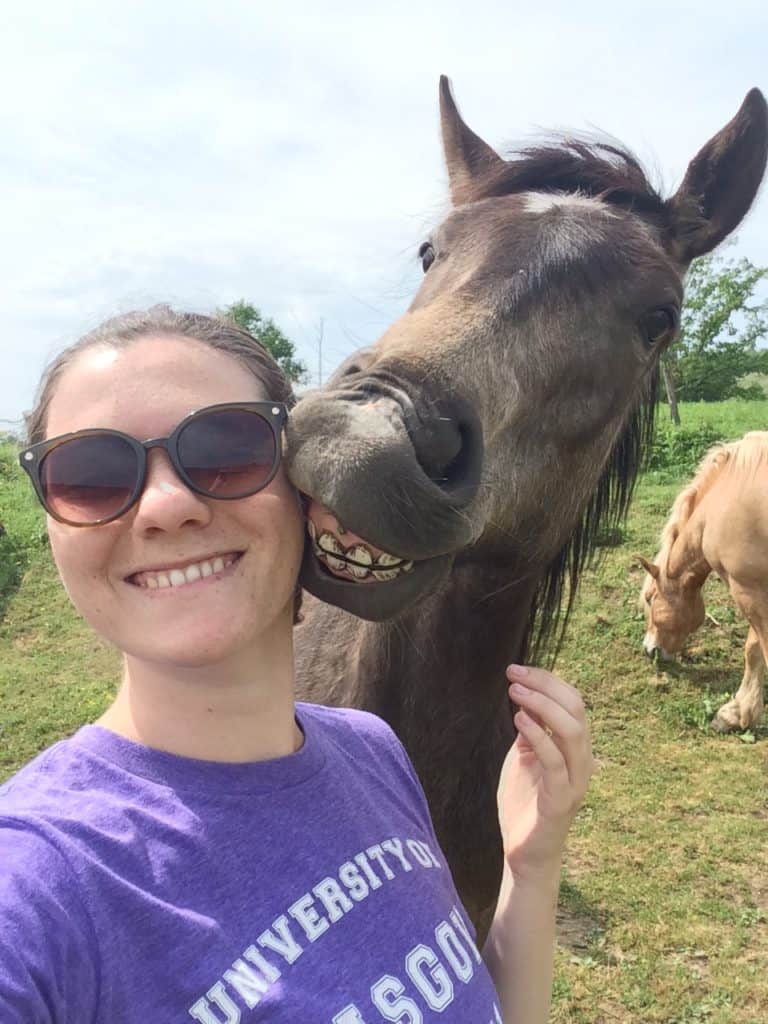 29 Greatest Ways to Make Money Travelling the World 11 Nina smiling at the camera with a horse over her shoulder baring its teeth