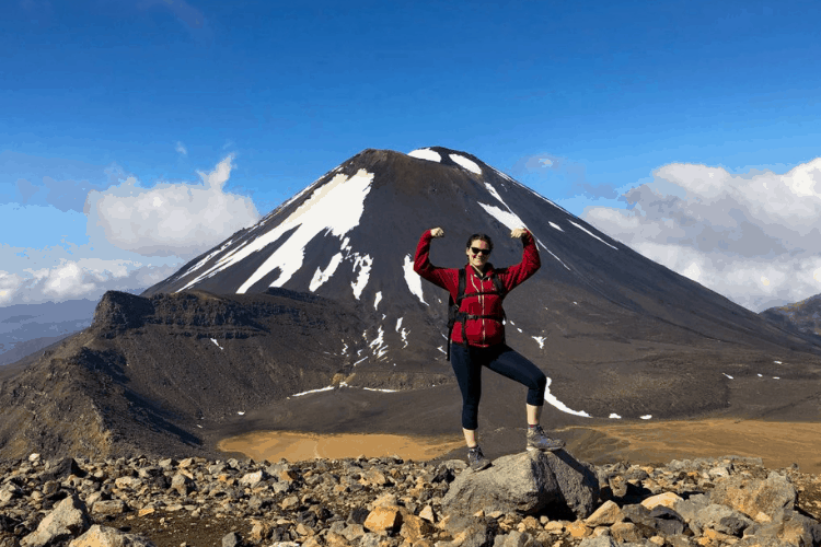 What to Wear Hiking: A Complete Guide for Beginners 1 What to Wear Hiking: photo of Nina a top a New Zealand mountain flexing her arms in front of a dormant volcano. Wearing a red sweater and cropped pants with hiking boots.