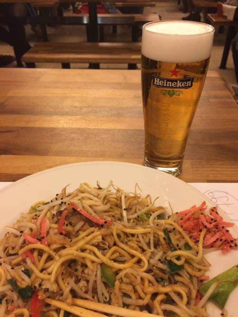 What You Need to Know Before Travelling to Amsterdam Alone 7 Heineken beer in a glass beside a thai dish on a wooden table to show the local beer that Nina tried on her trip alone to Amsterdam