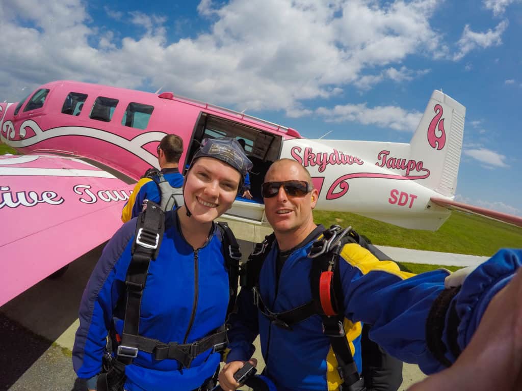 Skydiving in Taupo, New Zealand: 15,000 ft of Fun 2 Nina and her tandem instructor smiling at the camera in front of a pink airplane for Skydive Taupo