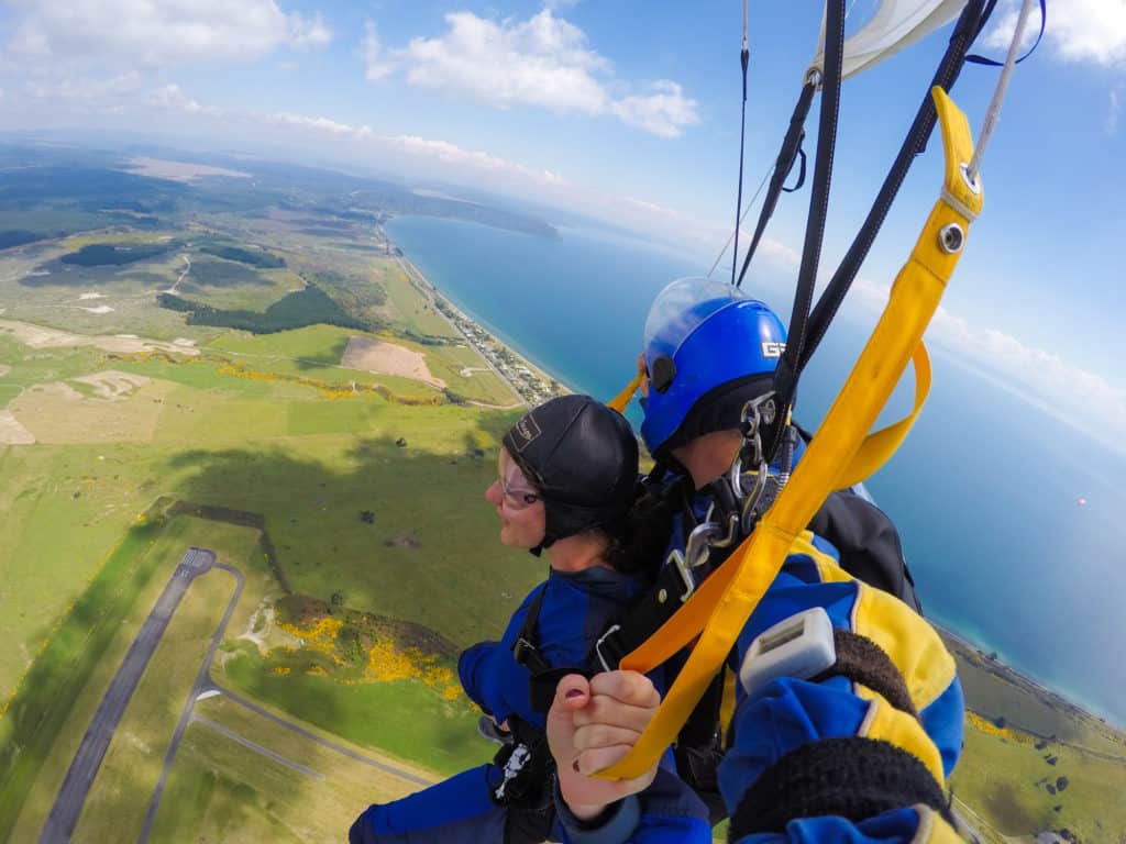 Skydiving in Taupo, New Zealand: 15,000 ft of Fun 12 Nina smiling overlooking the scenery of Taupo as she parachutes from her skydive with her tandem instructor behind her in New Zealand. Nina is controlling the parachute.