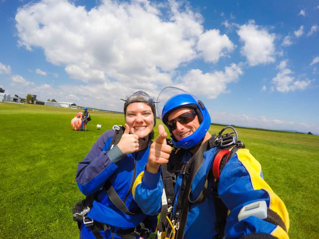 Skydiving in Taupo, New Zealand: 15,000 ft of Fun 17 Nina giving a thumbs up and Rhys shooting a finger gun at the camera as they smile after the skydive in New Zealand