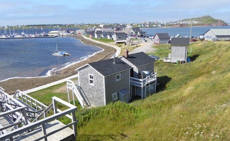 Best Quebec Road Trip (An Epic 2 Week Itinerary) 11 Grey beach houses alongside the shore of Magdalen Island with sailboats in the water. Quebec road trip idea for a destination.
