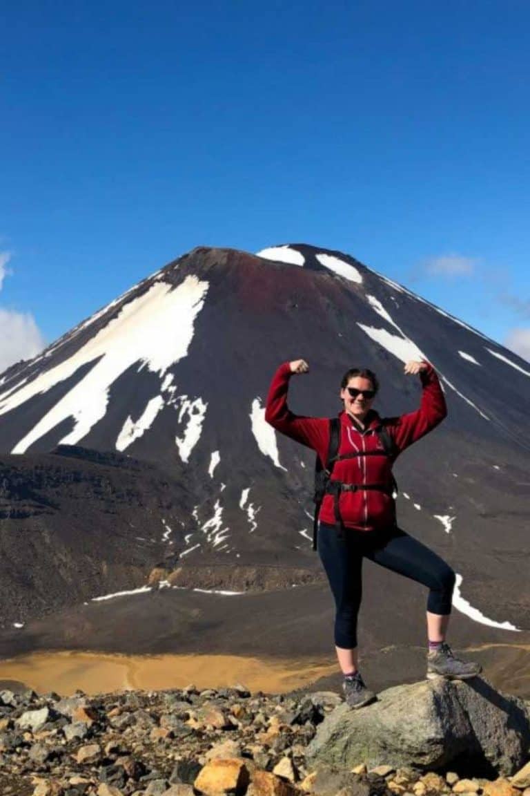 20 Pros and Cons of Solo Travel in 2024 from an Expert 39 Nina flexing on a mountain in front of a volcano in New Zealand