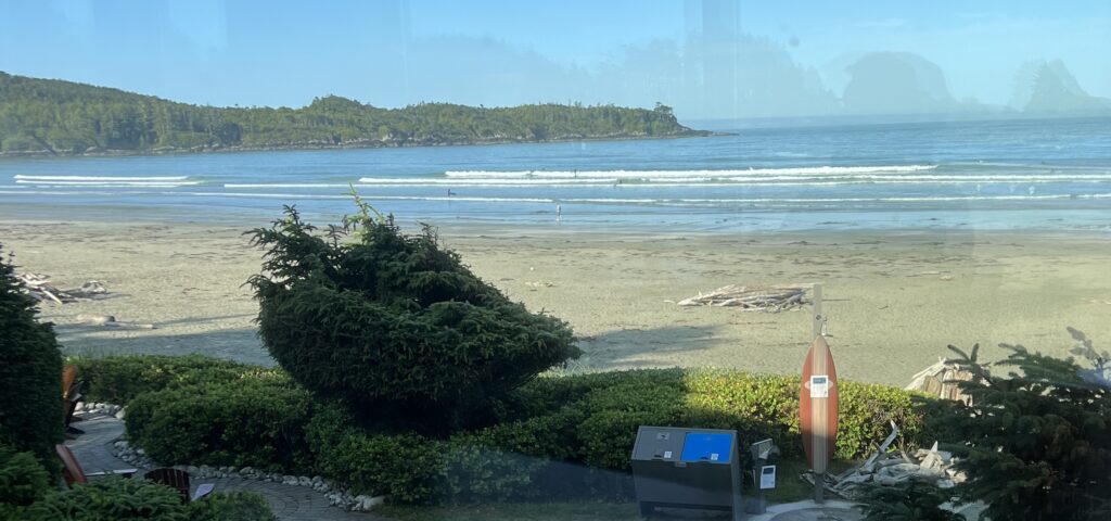 83 Bucket List Canada Things to Do in 2025 from a Canadian 26 View from a window overlooking Tofino's sandy beach and surf waves, framed by lush greenery, highlighting Canada's stunning Pacific coast.