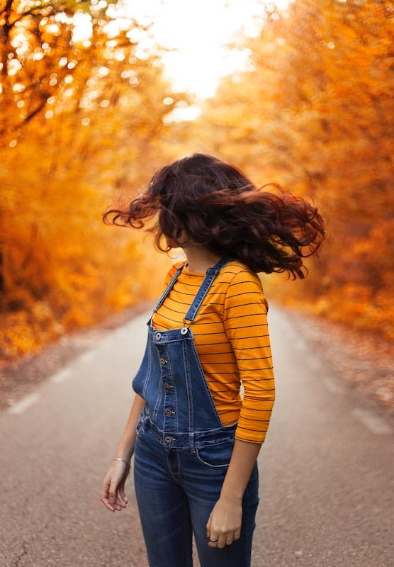 160 Best Fall Quotes and Captions for Instagram 2024 11 Woman turning with hair whipping in face against a golden fall foliage backdrop