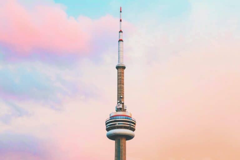 CN tower with a background of cotton candy looking clouds with light and dark pink clouds with a blue sky is a major pro of living in Toronto