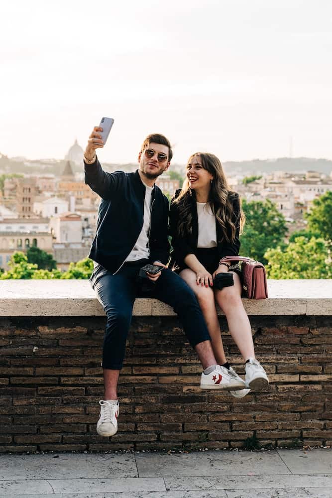 I Regret Moving to Another Country for Love: 7 Expat Stories 2 Couple smiling while sitting on an overlook and taking a selfie on tour abroad