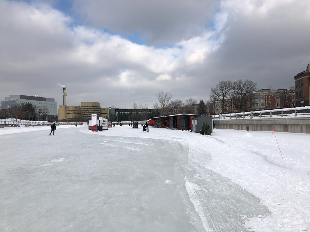 17 Reasons Not to Move to Canada in 2024 2 frozen river in canada on a gloomy cloudy day with a person ice skating down the river in the distance