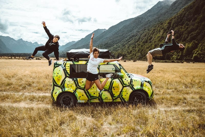 57 New Zealand Travel Tips (2024 Local's Guide) 11 Three friends jumping in front of a packed mini car in New Zealand's fjordland