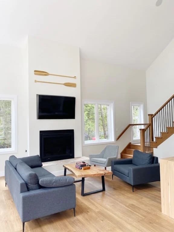 20 Top Airbnb Cottages in Muskoka for an Epic Getaway 29 Heart of 3-mile lake cottage view of the living room with electric fireplace and flat screen TV. Charcoal couches with pine flooring.