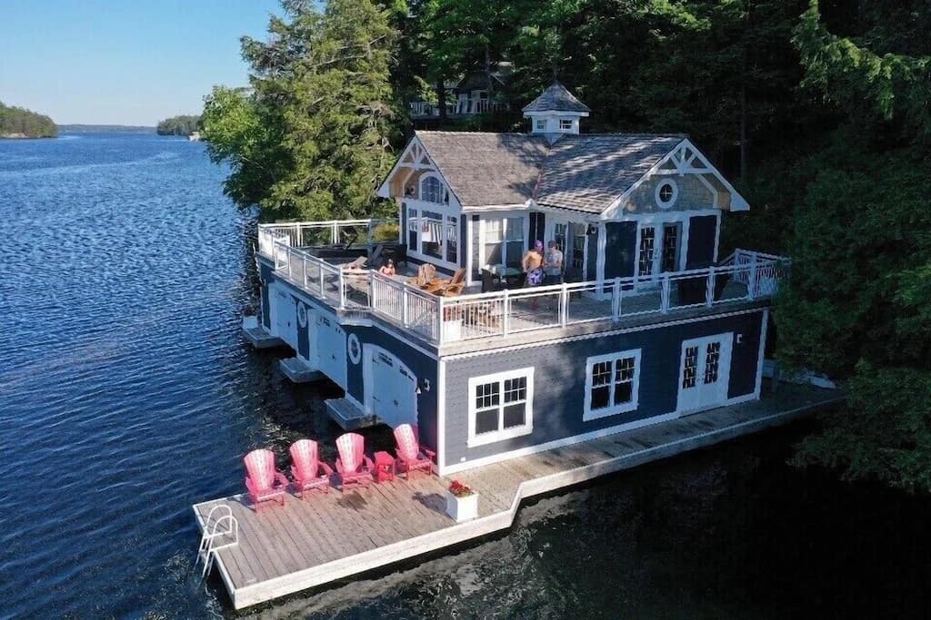 20 Top Airbnb Cottages in Muskoka for an Epic Getaway 52 Blue grey cottage compound on Lake Muskoka at this rental. Two story with white trim and three boat slips. Red muskoka chairs.