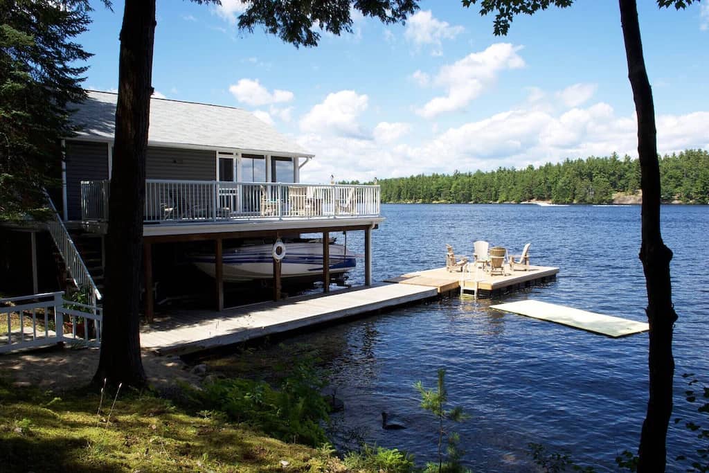 20 Top Airbnb Cottages in Muskoka for an Epic Getaway 46 Modern Executive Family Cottage boathouse and private dock. Lily pad in the water with yellow Muskoka chairs and wrap around porch on the boat house.