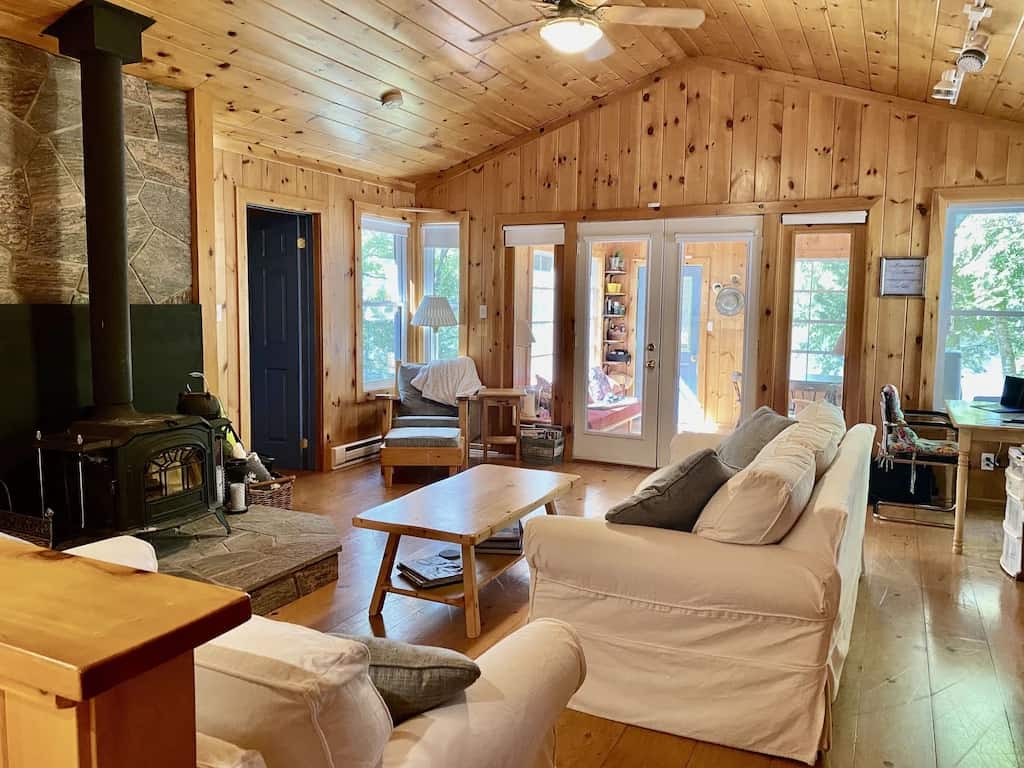 20 Top Airbnb Cottages in Muskoka for an Epic Getaway 35 Living room interior of the Moon River Retreat Airbnb. Wood burning fireplace with white couches and pine interior.