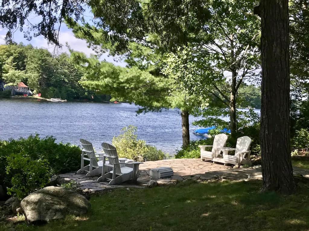 20 Top Airbnb Cottages in Muskoka for an Epic Getaway 34 Moon River lookout. View of the stone landing with four white Muskoka Chairs and pine trees on a sunny day.