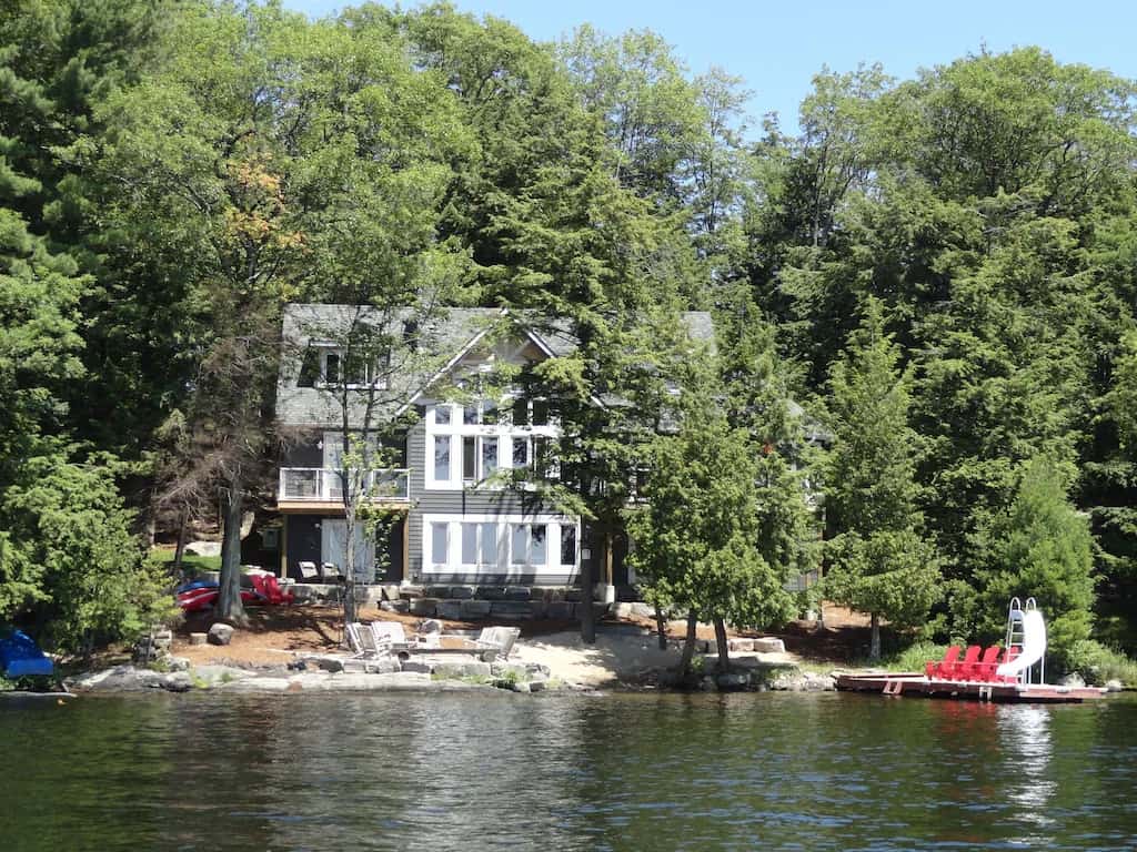20 Top Airbnb Cottages in Muskoka for an Epic Getaway 61 Pewter Muskoka Beach house exterior view showing the cottage and the dock with a water slide.