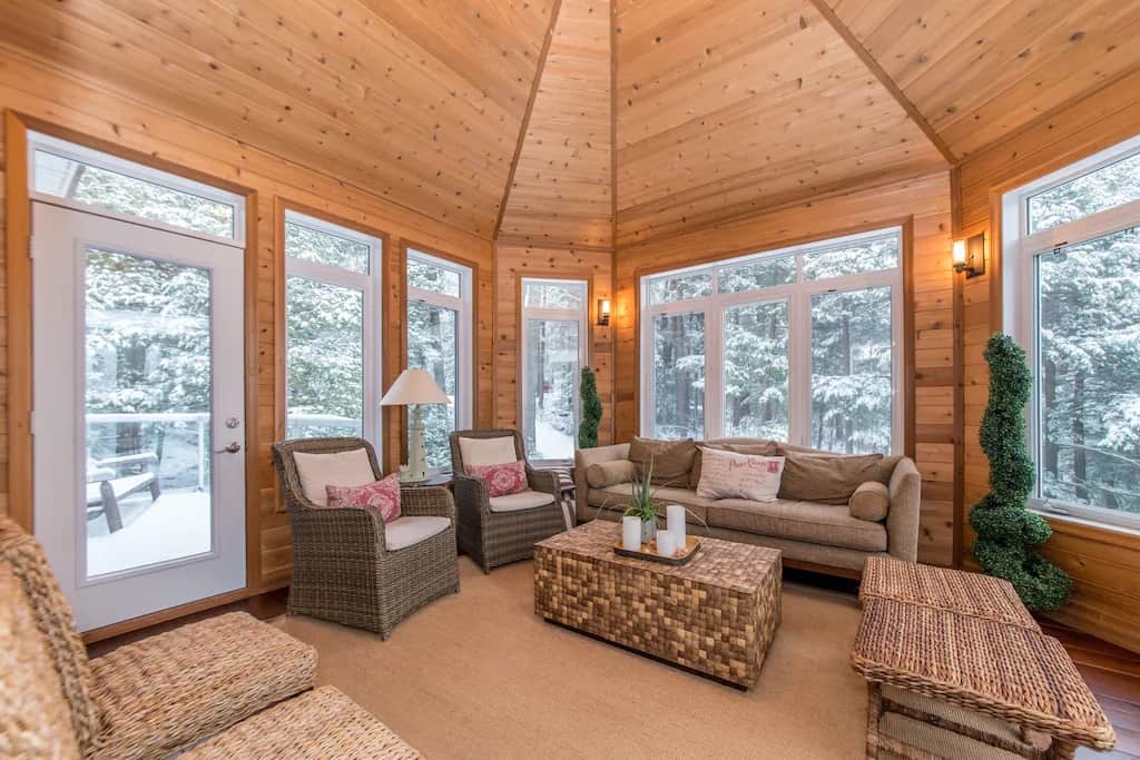 20 Top Airbnb Cottages in Muskoka for an Epic Getaway 63 Pine Muskoka room at the beach house. with light coloured furniture and wicker tables. Wrap around windows with view of the forest.