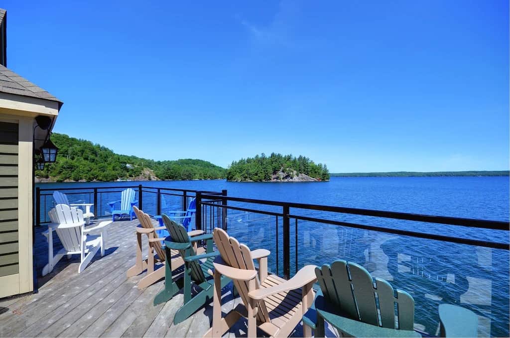 20 Top Airbnb Cottages in Muskoka for an Epic Getaway 31 Muskoka boathouse patio. Multi coloured Muskoka chairs on a glass patio overlooking Lake Muskoka