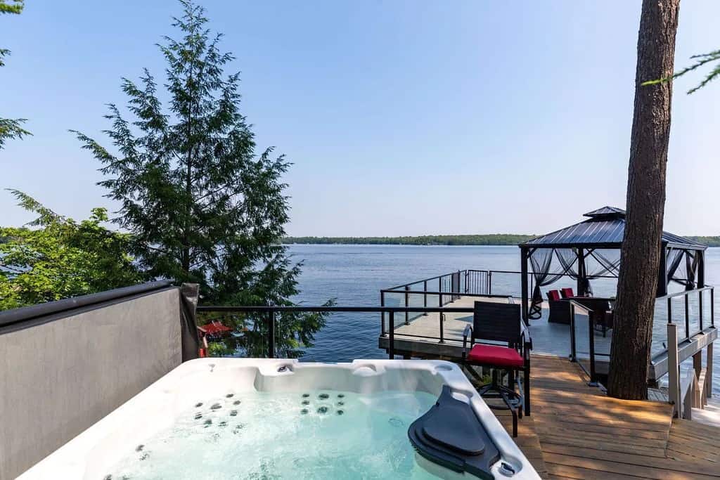 20 Top Airbnb Cottages in Muskoka for an Epic Getaway 42 View of hot tub on Lake Muskoka with a black gazebo and red couches outside.