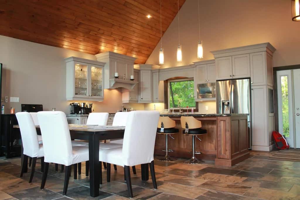 20 Top Airbnb Cottages in Muskoka for an Epic Getaway 22 New Luxury Cottage interior. View of the kitchen and dining room with modern amenities and a wood panelled ceiling.