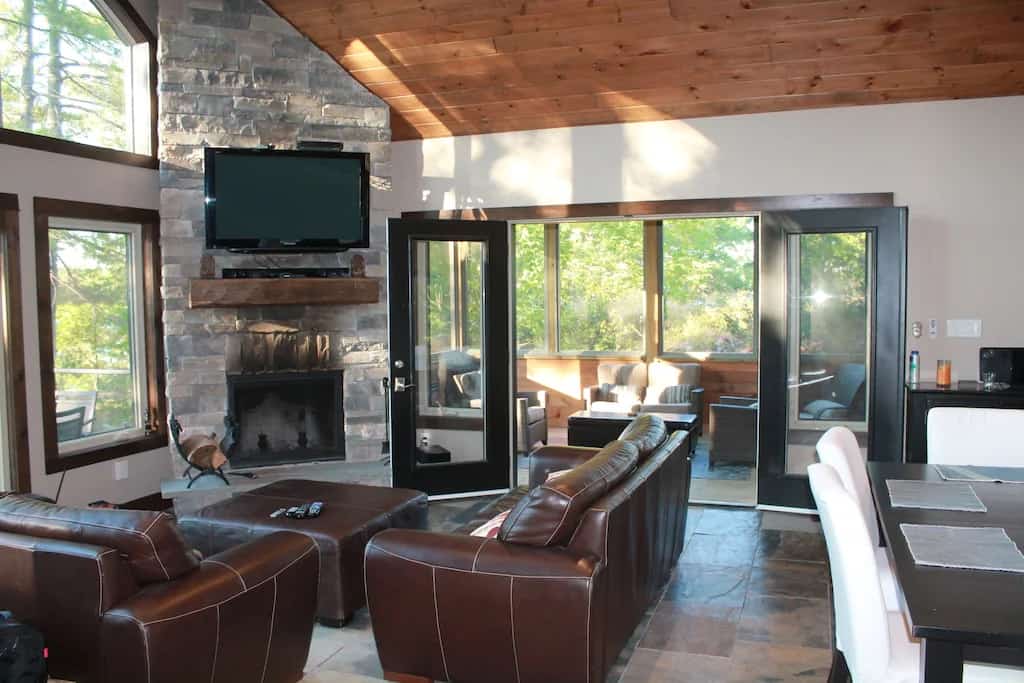 20 Top Airbnb Cottages in Muskoka for an Epic Getaway 23 New Luxury Cottage living room and Muskoka room. Flat screen mounted on a stone fireplace with brown leather couches.