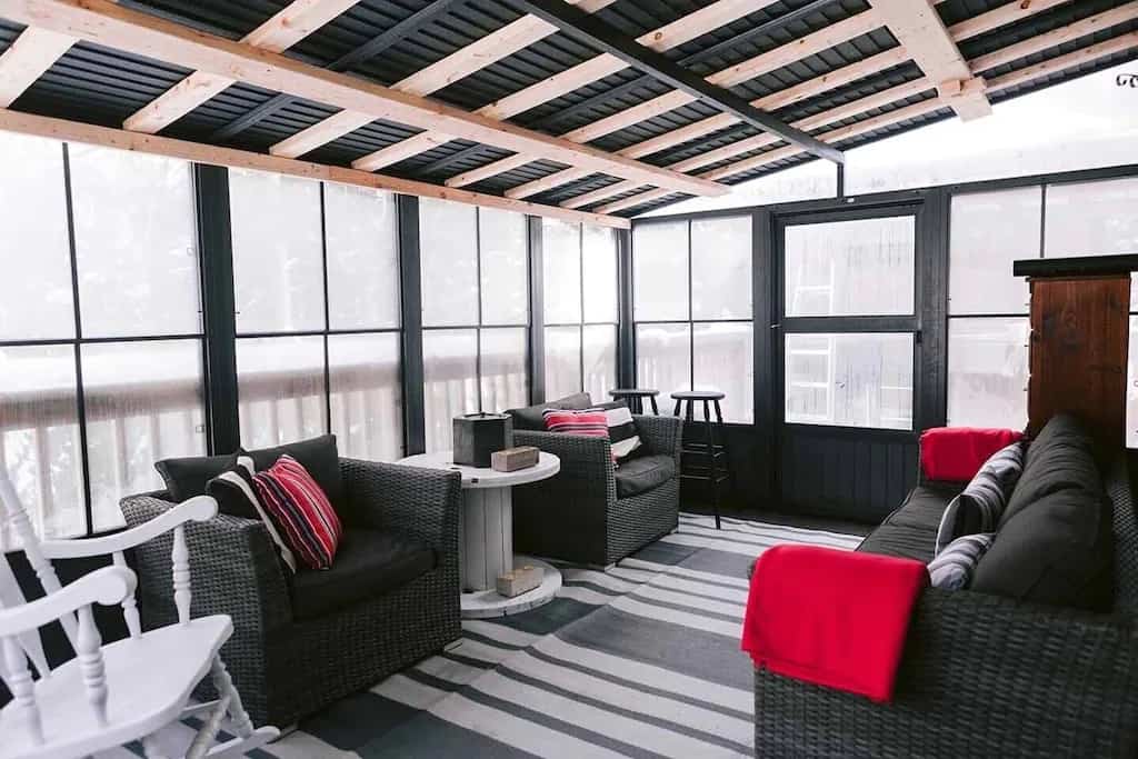 20 Top Airbnb Cottages in Muskoka for an Epic Getaway 17 Muskoka room at TuckAway cottage. Black couches with red pillows and post and beam ceilings.