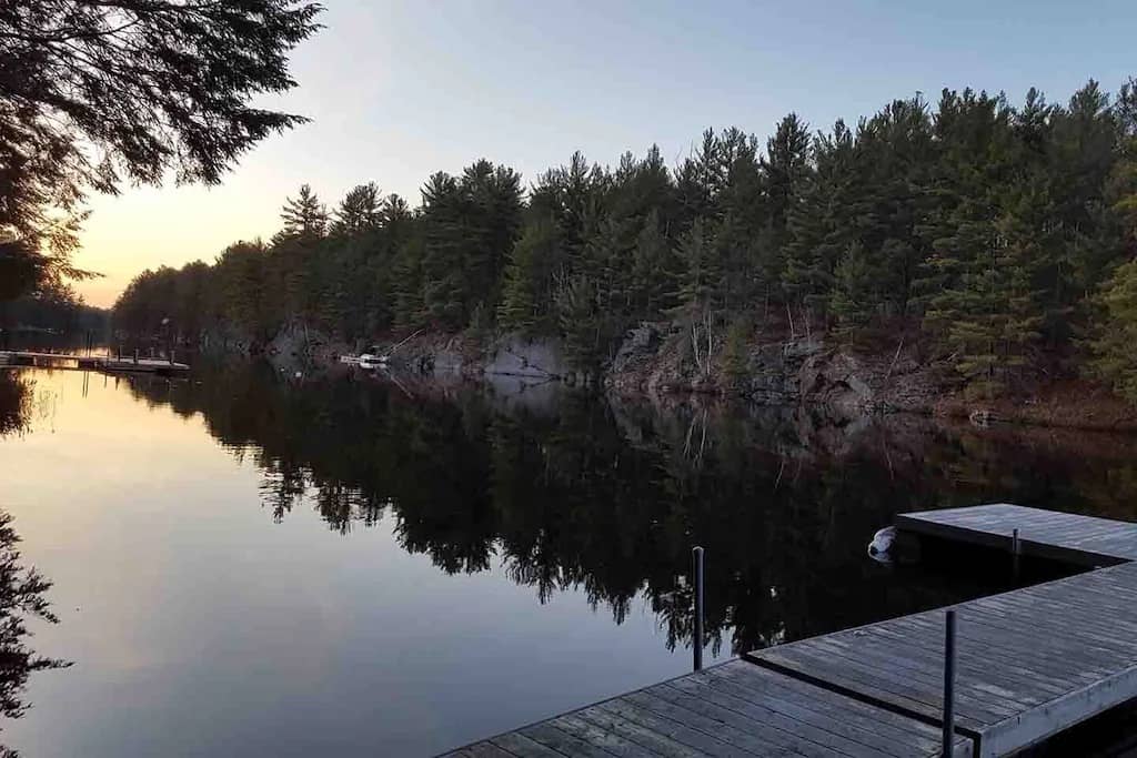20 Top Airbnb Cottages in Muskoka for an Epic Getaway 18 High Lake view from the dock at sunrise with pine trees surrounding the cottage.