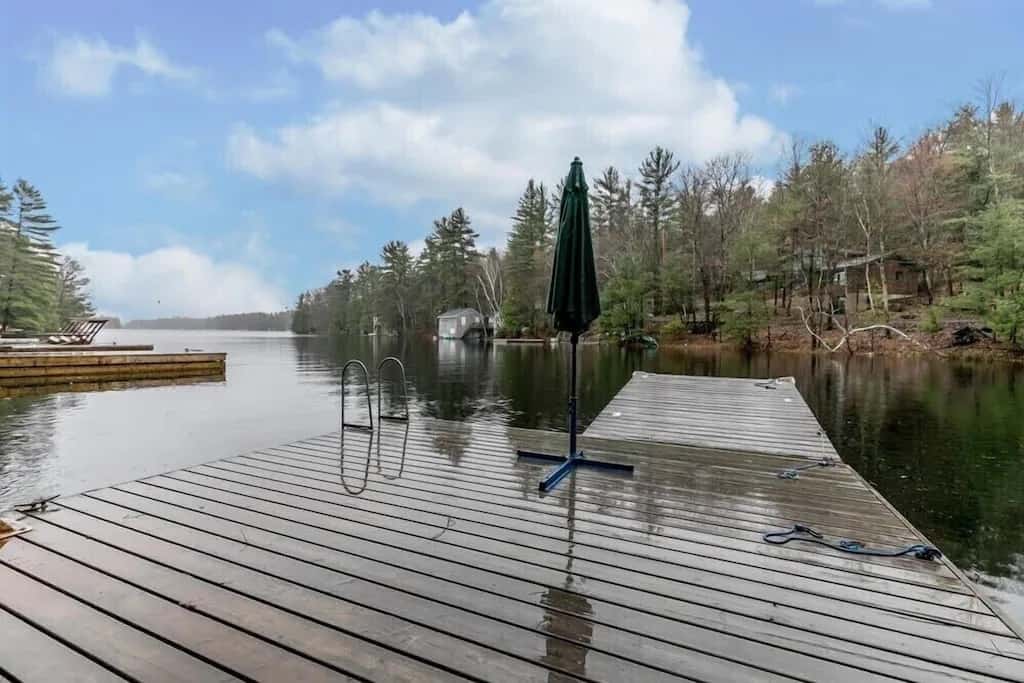 20 Top Airbnb Cottages in Muskoka for an Epic Getaway 6 Dock of the "Waterfront on Lake Muskoka" with pine trees surrounding the lake on a sunny day.