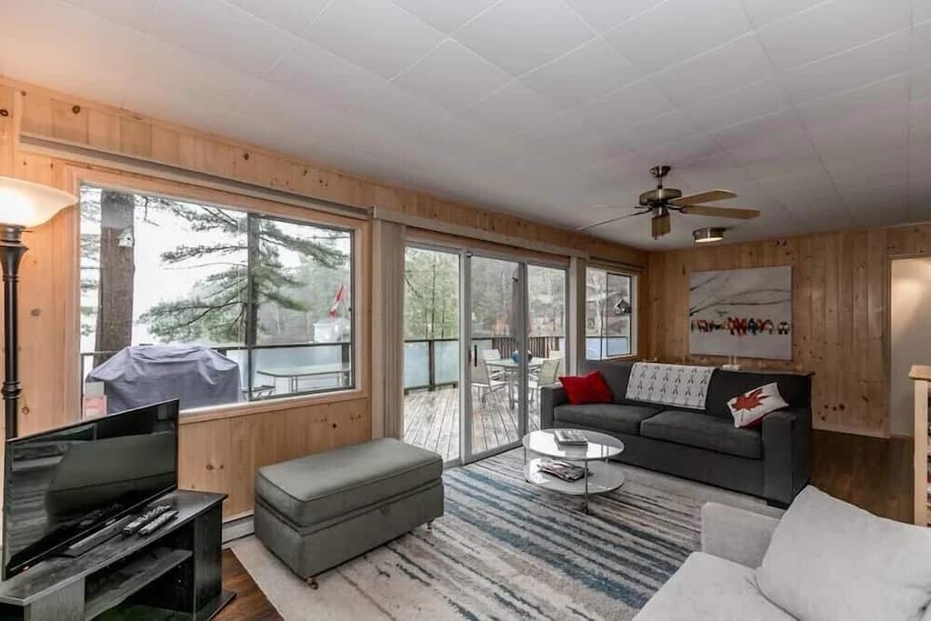 20 Top Airbnb Cottages in Muskoka for an Epic Getaway 5 Interior of the Waterfront on Lake Muskoka. Living room view with grey couches and wood walls, with a view of the patio.