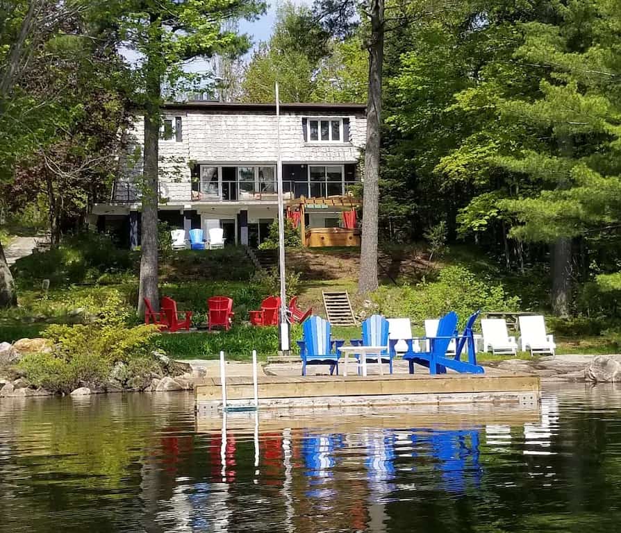 20 Top Airbnb Cottages in Muskoka for an Epic Getaway 56 Take a Week Off cottage exterior with private dock, seating area on patio, and white shaker cottage.