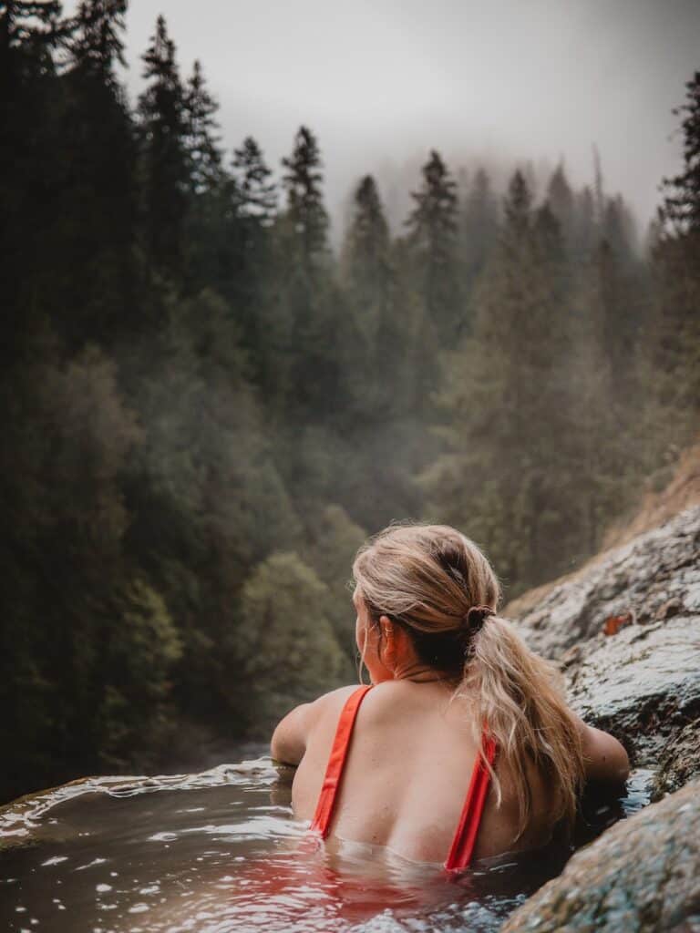 Canada in Autumn: 15 Reasons to Visit + Weather Guide 6 Woman soaking in a hot spring over looking the forest in Canada
