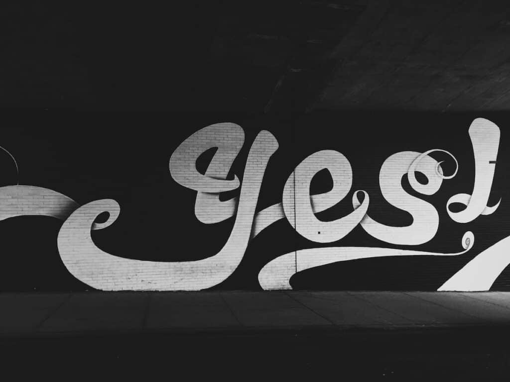 How to Say Yes and No in 100 Different Languages 4 Large "yes!" graffiti in white paint on a black brick wall in English